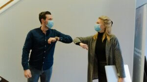 Two individuals with antiviral masks, elbow bumping in greeting