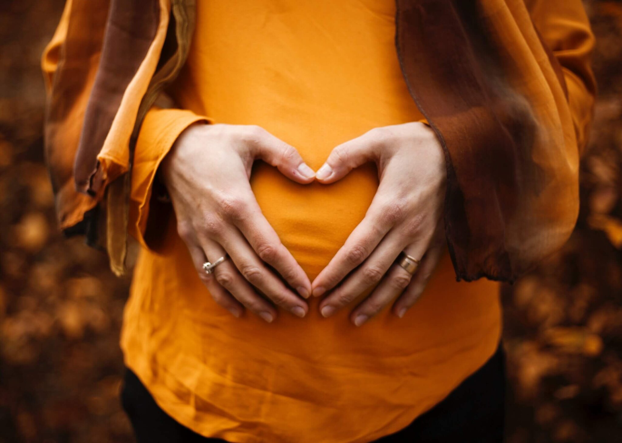 pregnant woman with orange shirt making a heart shape with her hands over her belly