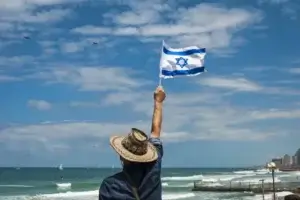 man standing on beach in tel aviv waving israeli flag