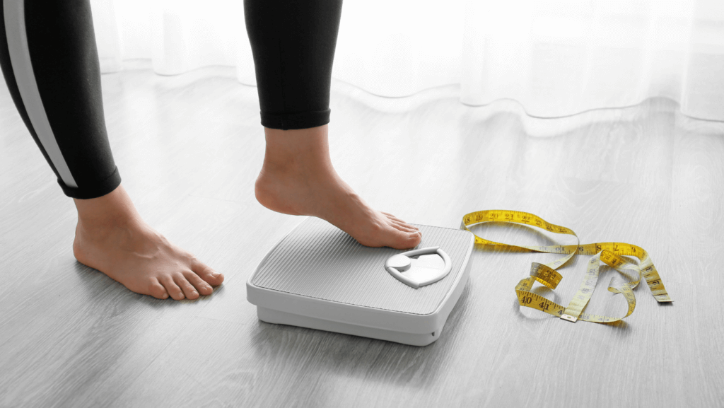 woman stepping onto a scale with measuring tape on the floor