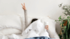 Women with outstretched arm flashing victory symbol from bed