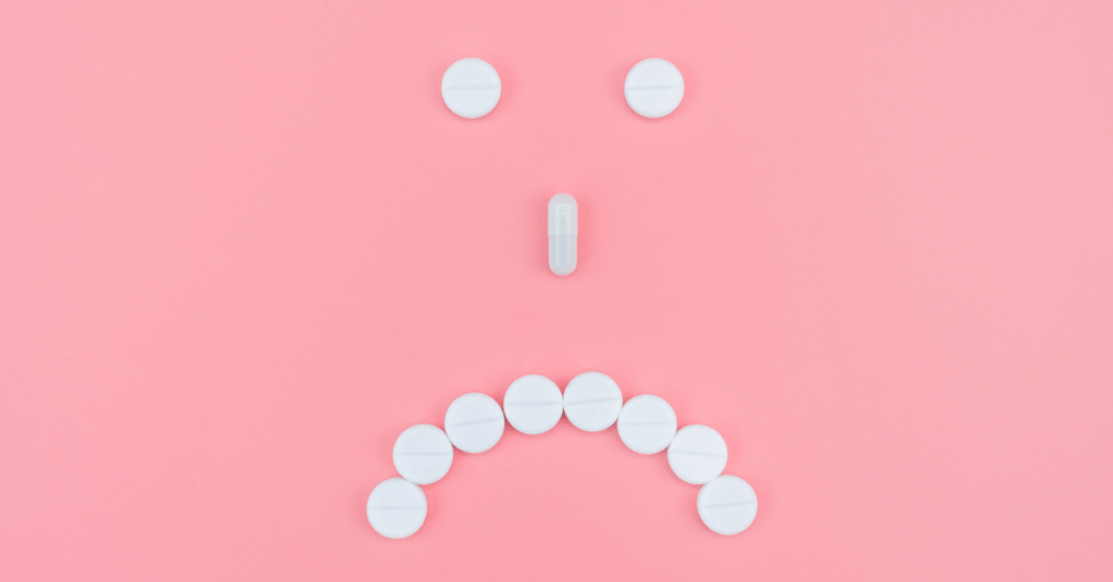 white pills organized in an unhappy face on pink background