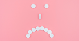 white pills organized in an unhappy face on pink background