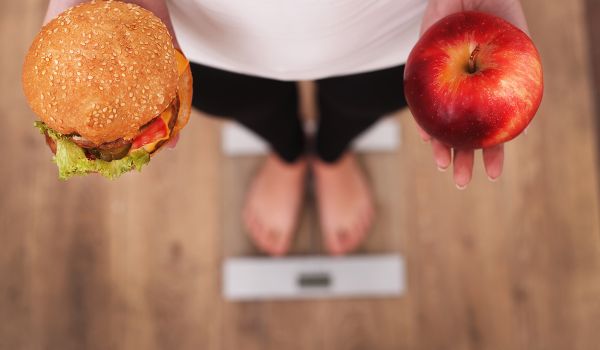 Woman on scale holding hamburger and apple