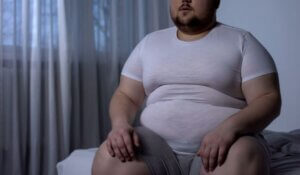 Overweight man sitting on bed, weight gain due to sedentary lifestyle, hormonal disease