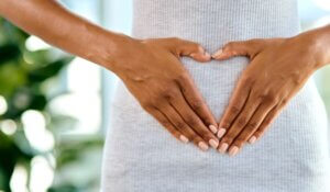 Woman with hands in heart shape around navel.