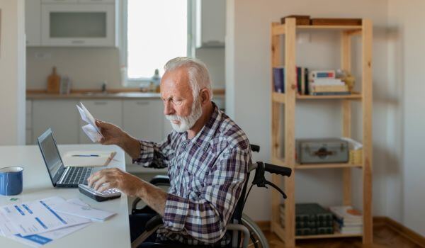Man in a wheelchair looks at his medication payments that he can't afford